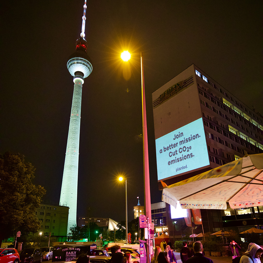 The Berlin TV Tower at night beside a building with a projected ‘Join a better mission. Cut CO₂e emissions.’ message